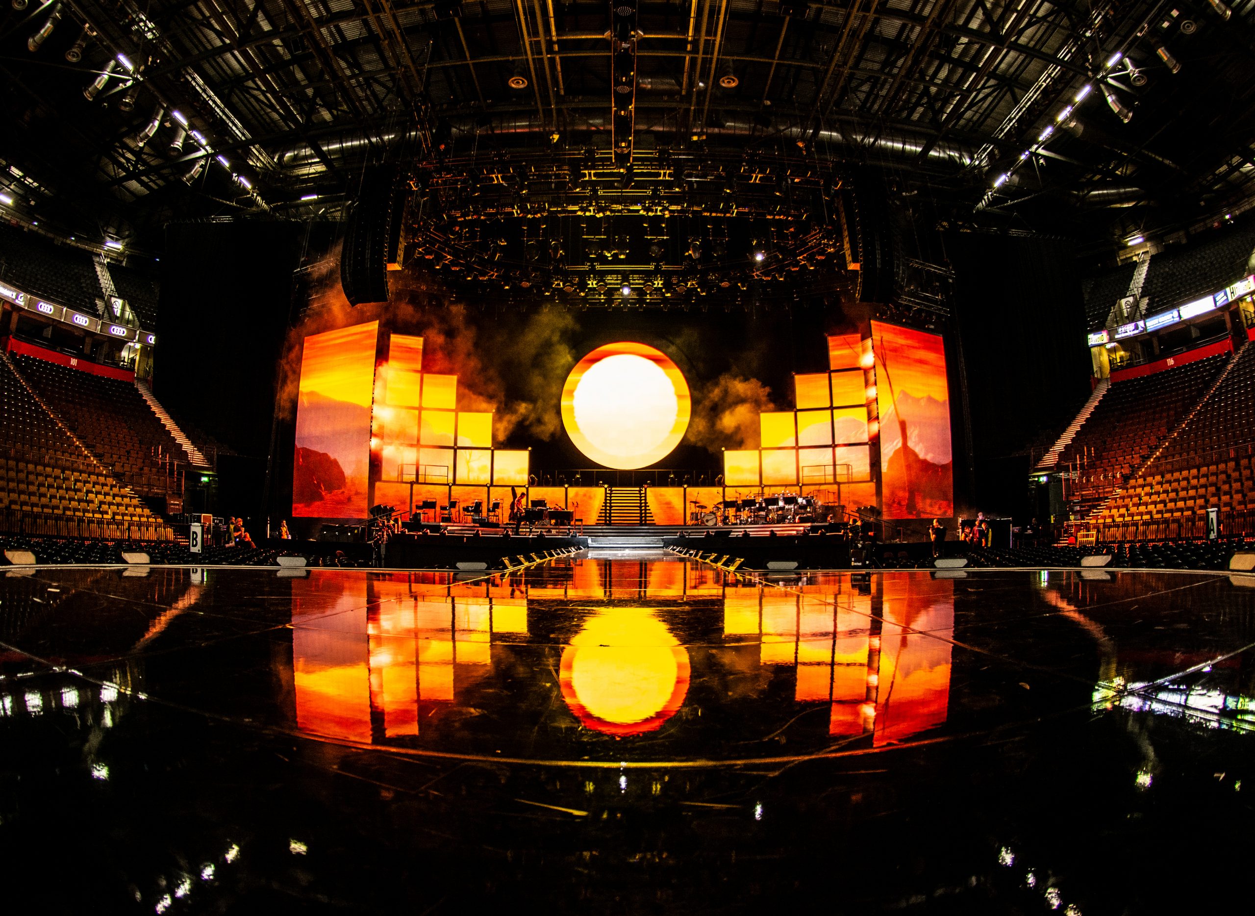 A dark stage with a bright light in the middle resembling the sun and Harlequin mirror effect flooring.