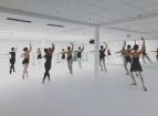 Female ballet dancers while practicing in front of a mirror in an all white ballet studio.